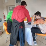 Uczeń w roli kelnera podaje zamówione jedzenie do stolika nakrytego białym obrusem.