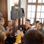 Grupa uczniów obsługuje starą maszynę drukarską.