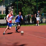 Dwóch chłopców ubranych na sportowo podczas meczu w piłkę nożną. W tle dzieci siedzące na trawie.