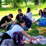 Grupa dzieci siedzi na kocach na trawie.