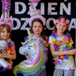 Trzy uśmiechnięte dziewczyny pozują do zdjęcia z balonami w kształcie jednorożców. W tle napis Dzień Dziecka.