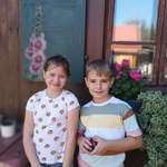 Dziewczynka i chłopiec pozują na tle wiejskiej chatki.jpg