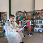 W bibliotece trójka uczniów klasy 8 czyta głośno książkę. Jeden z uczniów trzyma w dłoniach duże_ czerowne_ papierowe serce..jpg