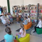 W bibliotece trójka uczniów klasy 8 czyta głośno książkę. Naprzeciwko nich na pufach siedzą uczniowie klasy 1b ..jpg