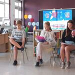 W bibliotece trójka uczniów klasy 8 czyta głośno książkę. W tle za nimi stoi duży ekran telewizora..jpg