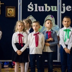 Grupa uczniów mówi wiersz. W tle widać napis ślubujemy.