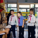 Trzech chłopców z klasy pierwszej przygląda się sztandarowi szkoły na korytarzu.