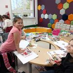 W bibliotece przy okrągłym stole siedzą uśmiechnięte uczennice. Na stole leżą kolorowe gazety..jpg