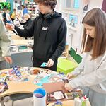 W bibliotece przy stole stoją uczniowie i wyklejają pracę Mapa marzeń.  W tle inni uczniowie wypożyczają książki..jpg