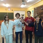 Szachści z SP 26 z medalami za trzecie miejsce stoją na tle szachwnic trzymając puchar.jpg