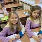 Dwie uśmiechnięte dziewczynki rozwiązują zadania na kartach pracy.jpg