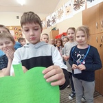 Uczeń przekłuwa szpilką imię przyszłej partnerki na papierowym sercu. W tle uczniowie obserwujący chłopca.jpg