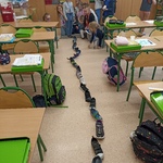 Uczniowie ustawiają swoje buty jeden za drugim -w przejściu między stolikami w klasie.jpg