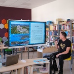 Zdjęcie 9 W bibliotece przy dużym ekranie siedzi pisarka i nauczyciel_  w tle półki z książkami..jpg