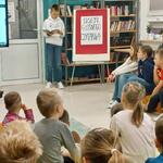 Zdjęcie 8 W bibliotece uczeń czyta wiersz_ Naprzeciwko na pufach i dywanie siedzą uczniowie_.jpeg