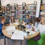 Zdjęcie 4 W bibliotece grupka uczniów siedzi przy okrągłym stole i wykonują prace plastyczne. W tle półki z książkami..jpg
