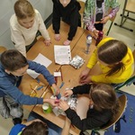 Dzieci pracują wspólnie przy stole nad projektem z wykorzystaniem papierowych kubków_ słomek i innych materiałów..jpg