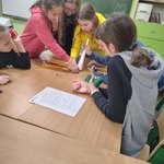 Dzieci pracują wspólnie przy stole nad projektem_ używając rurek_ papieru i instrukcji..jpg