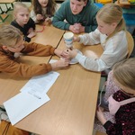Grupa dzieci siedzi przy stole i wspólnie pracuje nad projektem_ używając papierowego kubka oraz innych prostych materiałów..jpg