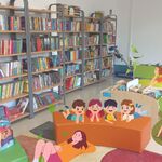 W bibliotece uczniowie leżą na pufach lub siedzą na dywanie. W tle półki z książkami. Pani nauczycielka czyta im bajkę..jpg