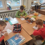 Chłopcy przy stolikach w klasie zaangażowani w rysowanie_ w otoczeniu przyborów szkolnych i pluszowych zabawek..jpg