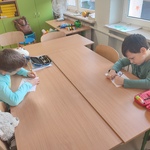 Dwóch chłopców w klasie pochylonych nad rysunkami_ obok nich leżą przybory szkolne i pluszowa zabawka..jpg