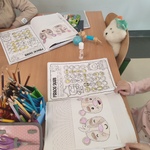 Otwarte zeszyty_ w których znajdują się kolorowe rysunki_ obok leżą kredki i pluszowa zabawka..jpg