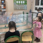 Dzieci bawią się w klasie szkolnej_ gdzie stół i krzesła zostały owinięte folią_ a dzieci malują po niej farbami..jpg