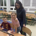 Chłopiec i dziewczynka wraz z nauczycielką sterują ustawionym na ławce pociągiem na torach..jpg