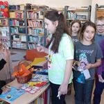 W bibliotece stoją uczennice_ losują karteczki z pytaniami konkursowymi.jpg