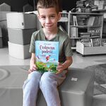 W bibliotece na pufie siedzi uczeń. Trzyma w rękach nagrodę książkową.jpg
