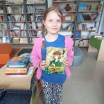 W bibliotece stoi uczennica_ trzyma w rękach nagrodę książkową.jpg