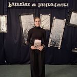 Uczennica stoi z książką w ręku. W tle czarna ściana z powieszonymi imitacjami luster..jpg