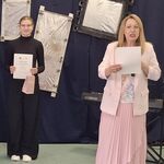 Uczennica stoi z dyplomem w ręku. W tle czarna ściana na której wiszą imitacje luster. Obok stoi pani z jury konkursu..jpg