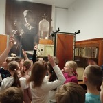 Dzieci zgłaszają się do odpowiedzi w czasie rozmowy z pracownikiem muzeum.jpg