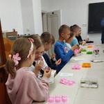 Uczniowie przy stolikach  sprawdzają wygląd i zapach utworzonych przez siebie mydełek.jpg