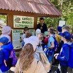 Przewodnik w Puszczy Knyszyńskiej mówi do dzieci_ w tle tablica z informacjami o leśnej edukacji przyrodniczej .jpeg