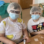 Dwaj chłopcy w maseczkach i czepkach ochronnych  wykonują proste czynności laboratoryjne..jpg