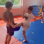 Dwóch chłopców na macie treningowej_ jeden z nich ćwiczy kopnięcie w tarczę trzymanego przez drugiego..jpg