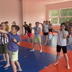 Grupa dzieci stojących na matach do ćwiczeń w sali treningowej_ wykonujących wspólne ruchy..jpg