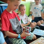 Chłopiec w czerwonej koszulce pokazuje kubek z nadrukiem_ siedząc wśród kolegów w klasie..jpg