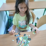 Dziewczynka w jasnozielonej koszulce układa na ławce elementy z motywami drogowymi i znakami..jpg