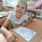 Dziewczynka z zieloną opaską uśmiecha się w ławce. Przed sobą ma kartę pracy z matematyki..jpg