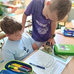 Dwaj chłopcy pracują razem w ławce nad kartą matematyczną_ otoczeni są przyborami szkolnymi..jpg