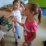 Dwie dziewczynki w klasie rozmawiają. Jedna w różowej koszulce gestykuluje_ druga trzyma kartkę..jpg