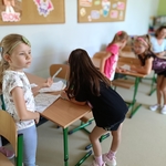 Dzieci w klasie pracują przy ławkach_ wypełniając karty i rozmawiając ze sobą..jpg