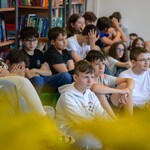 W bibliotece uczniowie siedzą na dywanie. W tle półki z książkami..jpg