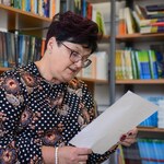 W bibliotece Pani Dyrektor siedzi na fotelu i czyta fraszkę. W tle półki z książkami..jpg