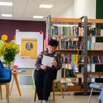 W bibliotece Pani Dyrektor siedzi na fotelu i czyta fraszkę. W  tle pólki z książkami_ stolik z kwiatami..jpg