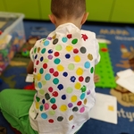 Chłopiec w koszulce w kolorowe kropki siedzi na dywanie i bawi się klockami edukacyjnymi..jpg